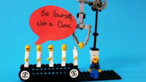 Image of identical lego people on a conveyor belt with the words "be yourself, not a clone" written on a speech bubble.