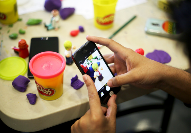Image of a person on a phone taking a photo of a lego person and play-doh as part of a workshop activity.
